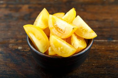 Ahşap arka planda bir kasede dilimlenmiş sarı domates. Sebze, malzeme ve zımba. Sağlıklı yemek..