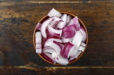 Ahşap arka planda bir kasede dilimlenmiş kırmızı soğan. Sebze, malzeme ve zımba. Sağlıklı yemek..