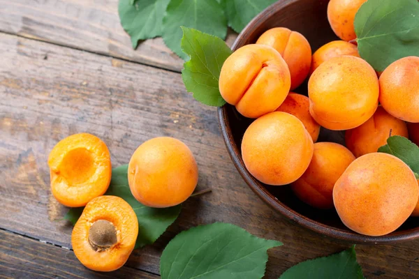 Ahşap bir zeminde, bir masada, kil bir tabakta olgun kayısılar. Kayısıların yanında yeşil izin.