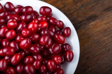 Ahşap bir arka planda beyaz bir tabakta köpek ahşabı. Yaz hasadını topluyorum. Kırmızı çilek.