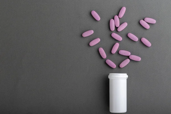 Oval pink pills are poured from a jar on a gray background. Space for text.