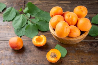 Ahşap arka planda, masanın üzerinde, ahşap bir tabakta olgun kayısılar. Kayısıların yanında yeşil izin.