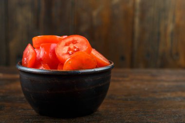 Ahşap arka planda bir kasede dilimlenmiş kırmızı domates. Sebze, malzeme ve zımba. Sağlıklı yemek..
