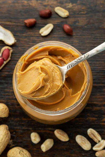 peanut paste in an open jar and peanuts in the peel scattered on the table