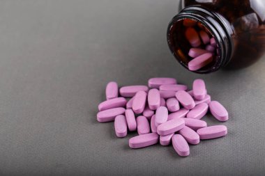 Eflatun tıbbi haplar gri arka planda şişeden dökülüyor. Sağlık kavramı, uyuşturucu bağımlılığı. Metin için boşluk.