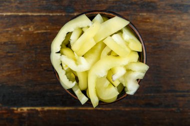 Ahşap arka planda bir kasede dilimlenmiş çiğ sarı biber. Sebze, malzeme ve zımba. Sağlıklı yemek..