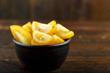 Ahşap arka planda bir kasede dilimlenmiş sarı domates. Sebze, malzeme ve zımba. Sağlıklı yemek..