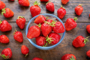 Ahşap bir masada cam bir kasede çilekler..