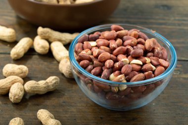 Cam bir kasede soyulmuş fıstık ve ahşap bir masada soyulmamış..