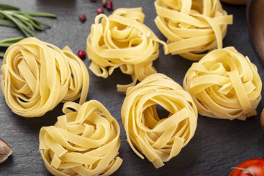 Çiğ makarna tagliatelle taze domates, biber, kuşkonmaz fasulyesi, baharat ve peynirli siyah masa. İtalyan spagettisi için yemek malzemeleri..