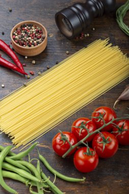 Taze domatesli çiğ makarna, biber, kuşkonmaz fasulyesi, baharat ve peynir ahşap bir masada. İtalyan spagettisi için yemek malzemeleri..
