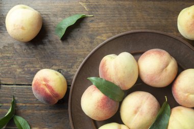 Tahta bir masada, kil bir tabakta yapraklarla olgunlaşmış şeftaliler. Taze hasat. Üst görünüm.