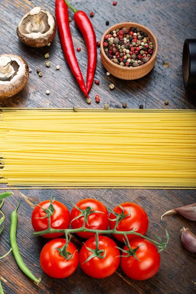 Taze domatesli çiğ makarna, biber, kuşkonmaz fasulyesi, baharat ve peynir ahşap bir masada. İtalyan spagettisi için yemek malzemeleri..
