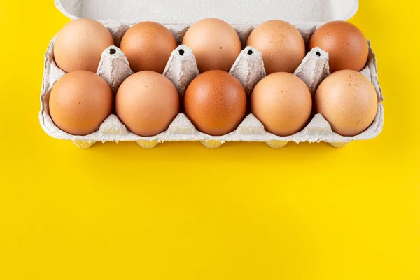 Chicken eggs in an open egg carton isolated on yellow. Top view with copy space. Natural healthy food and organic farming concept.