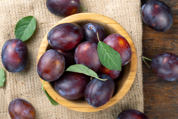 Спелые сливы и листья в деревянной чаше на столе. Сезон сбора урожая. Вид сверху.