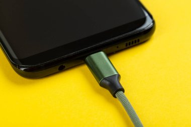 Sarı arka planda bir cep telefonunu şarj etmek.