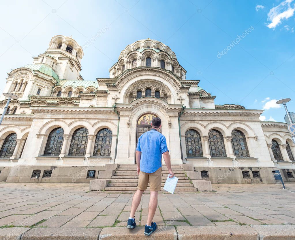 Young caucasian man with a map visiting Alexander Nevsky cathedral in Sofia, Bulgaria. Solo traveler concept.