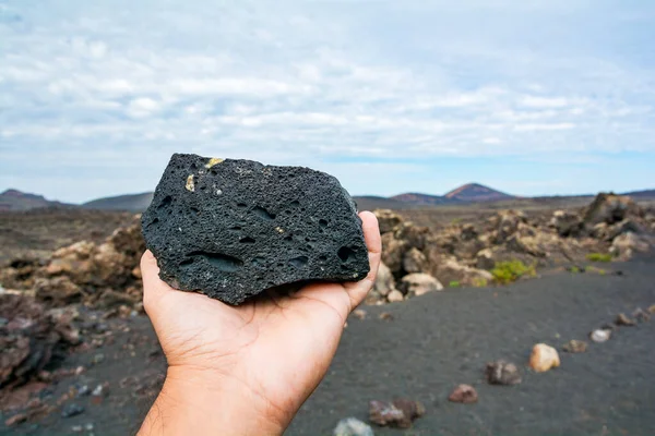 Hand holding a lava stone and a volcano in the background.