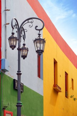 Buenos Aires'te, Arjantin'in La Boca semtinde, mavi gökyüzüne karşı eski duvarlara sahip bir sokak lambasının ve renkli binaların dikey görünümü.