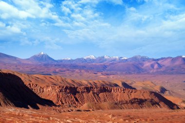 San Pedro de Atacama yakınlarındaki kırmızı kayalık oluşumlar ve volkanlar Çöl manzara, Şili, bulutlar ile kaplı mavi bir gökyüzüne karşı.