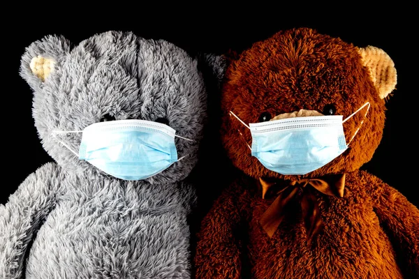 Two teddy bears wearing face masks isolated on a black background