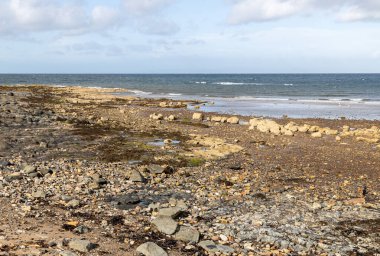 Kiremit manzarası ve kayalık plaj gelgitler ve yazları mavi bulutlu gökyüzü.