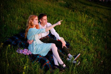 Genç çift, park ve günbatımı bakmak ekose oturan kadın ufuk işaret ediyor.