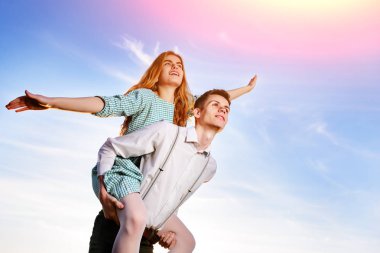 Genç adam neşeli kız arkadaş gibi gökyüzü arka plan üzerinde uçak piggybacking.