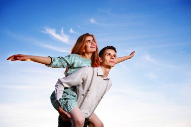 Genç adam neşeli kız arkadaş gibi gökyüzü arka plan üzerinde uçak piggybacking.