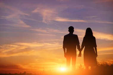young couple is holding hands on a background sunset silhouette. clipart