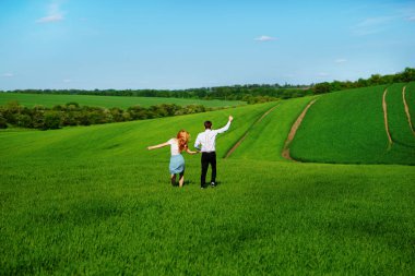Mutlu aşıklar çayır yeşil çim ve arkasından mavi gökyüzü ile çalışan.