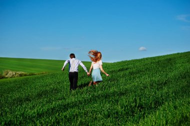 Mutlu aşıklar çayır yeşil çim ve arkasından mavi gökyüzü ile çalışan.