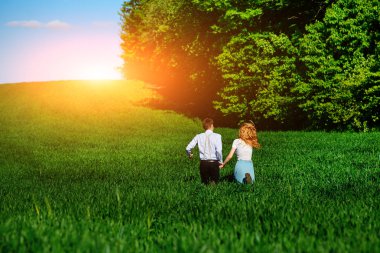 Mutlu aşıklar çayır yeşil çim ve arkasından mavi gökyüzü ile çalışan.