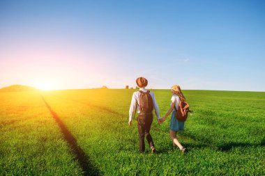 Bir sırt çantası ile bir adam bir şapka ve uzun saçlı bir kadın yol boyunca gidin. Çayır boyunca birkaç yürür.