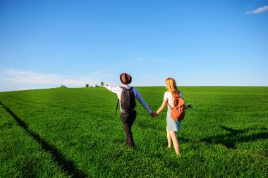 Bir sırt çantası ile bir adam bir şapka ve uzun saçlı bir kadın yol boyunca gidin. Çayır boyunca birkaç yürür.