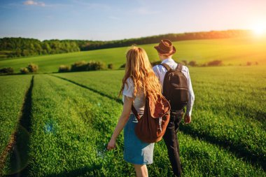 Bir sırt çantası ile bir adam bir şapka ve uzun saçlı bir kadın yol boyunca gidin. Çayır boyunca birkaç yürür.