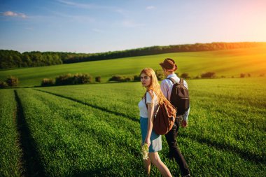 Bir sırt çantası ile bir adam bir şapka ve uzun saçlı bir kadın yol boyunca gidin. Çayır boyunca birkaç yürür.