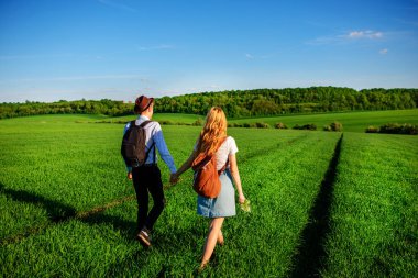 Bir sırt çantası ile bir adam bir şapka ve uzun saçlı bir kadın yol boyunca gidin. Çayır boyunca birkaç yürür.
