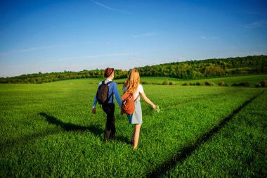 Bir sırt çantası ile bir adam bir şapka ve uzun saçlı bir kadın yol boyunca gidin. Çayır boyunca birkaç yürür.
