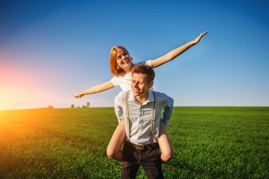 Kollarını dışarı çeker ve arka planı mavi gökyüzü ve yeşil alan bir uçuş taklit eder onun geri mutlu kadın, erkek gülümseyen holding.
