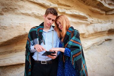 Güzel kadın ve yakışıklı bir battaniyeye sarılmış. Onlar gülümseyen ve bir tablet ekranında bir kum ocağı arka plan üzerinde seyir.