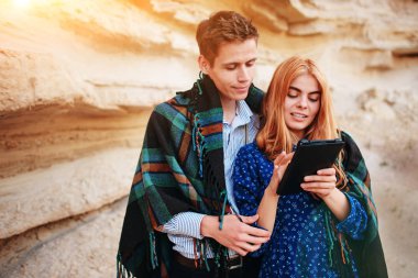 Güzel kadın ve yakışıklı bir battaniyeye sarılmış. Onlar gülümseyen ve bir tablet ekranında bir kum ocağı arka plan üzerinde seyir.