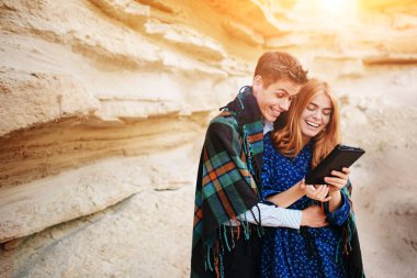 Güzel kadın ve yakışıklı bir battaniyeye sarılmış. Onlar gülümseyen ve bir tablet ekranında bir kum ocağı arka plan üzerinde seyir.