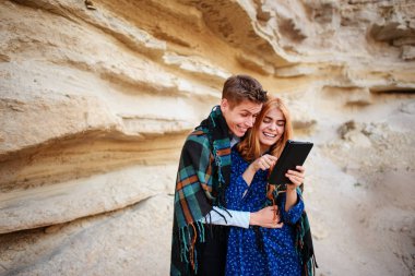 Güzel kadın ve yakışıklı bir battaniyeye sarılmış. Onlar gülümseyen ve bir tablet ekranında bir kum ocağı arka plan üzerinde seyir.