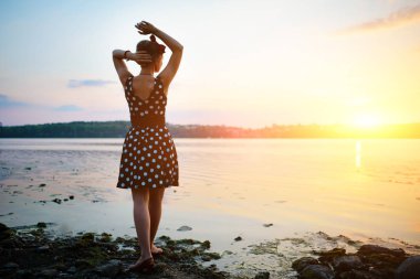 Gün batımını arka plan üzerinde göl kenarında duran giymiş kadın çok güzel genç.