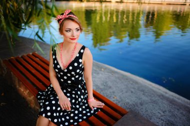 Güzel bir genç kadın giyinmiş gölet yakınındaki bir bankta oturur.