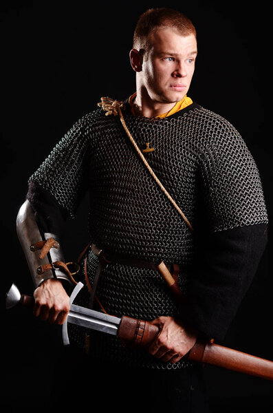 A soldier in a chain of letters stands with a sword in his hands on a black background.