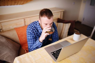 onun laptop Internet sörf ve viski içme cam genç profesyonel.