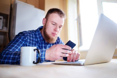 Ofiste cama tabloda, dizüstü bilgisayar ve akıllı telefon kullanan adam.