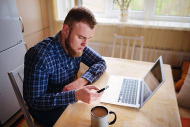 Ofiste cama tabloda, dizüstü bilgisayar ve akıllı telefon kullanan adam.